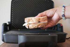 een persoon is ophalen een gegrild belegd broodje van de rooster foto
