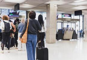 vrouw met bagage staand in een lijn Bij luchthaven. foto