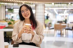 een mooi jong Aziatisch vrouw in gewoontjes slijtage is zittend in een koffie winkel in de boodschappen doen winkelcentrum. foto