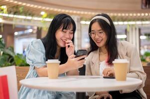 twee Aziatisch vrouw vrienden zijn ontspannende in een cafe in de boodschappen doen winkelcentrum na boodschappen doen samen. foto