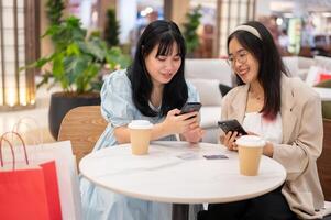 twee Aziatisch vrouw vrienden zijn ontspannende in een cafe in de boodschappen doen winkelcentrum na boodschappen doen samen. foto