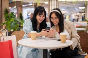twee Aziatisch vrouw vrienden zijn ontspannende in een cafe in de boodschappen doen winkelcentrum na boodschappen doen samen. foto