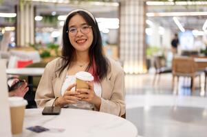 een mooi jong Aziatisch vrouw in gewoontjes slijtage is zittend in een koffie winkel in de boodschappen doen winkelcentrum. foto
