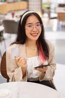 een vrouw is tonen haar credit kaart naar de camera terwijl zittend in een restaurant in een boodschappen doen winkelcentrum. foto