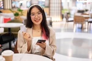 een vrouw is tonen haar credit kaart naar de camera terwijl zittend in een restaurant in een boodschappen doen winkelcentrum. foto