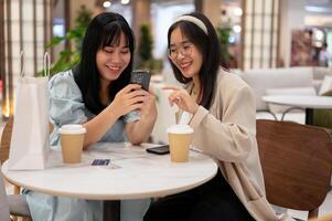 twee Aziatisch vrouw vrienden zijn genieten van pratend terwijl zittend samen in een cafe in de boodschappen doen winkelcentrum. foto