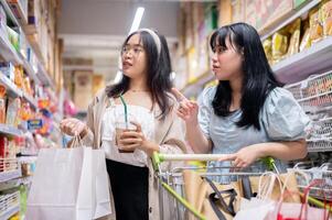 twee jong Aziatisch Dames winkel samen in een kruidenier op te slaan, gefocust Aan selecteren items van de planken. foto