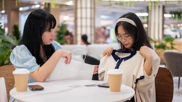 twee Aziatisch Dames zitten in een cafe Bij een winkelcentrum, een opgewonden tonen uit een nieuw overhemd naar haar vriend. foto