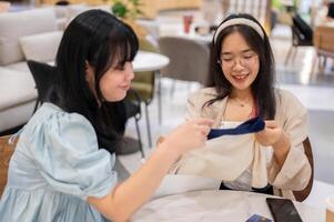 twee Aziatisch Dames zitten in een cafe Bij een winkelcentrum, een opgewonden tonen uit een nieuw overhemd naar haar vriend. foto