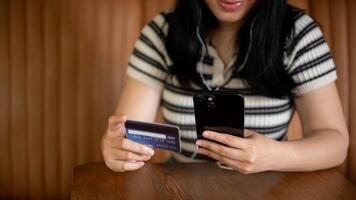 een bijgesneden beeld van een Aziatisch vrouw Holding een smartphone en een credit kaart Bij een tafel in een koffie winkel foto