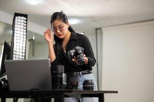 een aantrekkelijk Aziatisch vrouw fotograaf is controle afbeeldingen Aan haar laptop, werken in een studio. foto