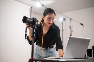 koel, professioneel Aziatisch vrouw fotograaf is controle afbeeldingen Aan haar laptop, werken in de studio foto