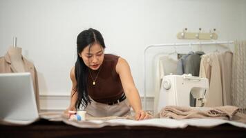 een professioneel Aziatisch vrouw mode ontwerper of kleermaker is scherpstellen Aan haar werk in de atelier studio foto