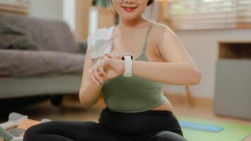 een fit Aziatisch vrouw in sportkleding is controle haar hart tarief en verbrand calorieën Aan haar smartwatch. foto