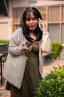 een mooi Aziatisch vrouw is pratend Aan de telefoon met iemand terwijl wandelen in de stad. foto