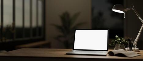 een hedendaags kantoor Bij nacht Kenmerken een wit scherm laptop computer mockup Aan een houten bureau. foto