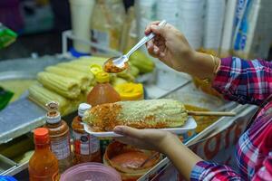 Mexicaans vrouw voorbereidingen treffen een gekookt maïs, typisch Mexicaans straat voedsel. voedsel kraam. elote. foto