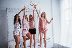 confetti in de lucht. jonge meisjes hebben plezier op het witte bed in een mooie kamer foto