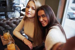 op de langgerekte hand. jonge vriendinnen nemen selfie in het restaurant met twee gele drankjes op tafel foto