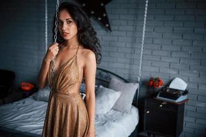 geketend bed. meisje in gouden jurk staat voor wit bed in luxe appartementen foto