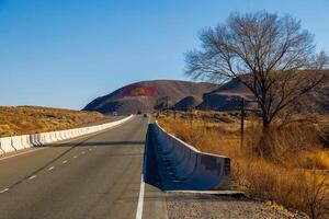 een weg met beton barrière kronkelend door natuurlijk landschap. de vlag van Kirgizië is getrokken Aan een berg Bij zonnig herfst dag. foto