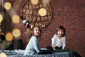 zorgeloze glimlach. kleine meisjes die plezier hebben op het bed met vakantie-interieur op de achtergrond