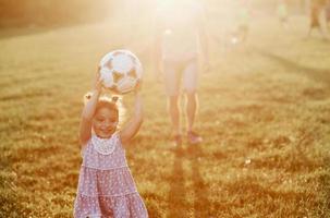 schattig klein meisje wordt verliefd op voetbal. papa's hobby kan voor twee van hen een goed humeur creëren foto