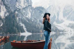 schoonheid van de natuur en meisje in één foto. vrouw in zwarte hoed genietend van majestueus berglandschap in de buurt van het meer met boten