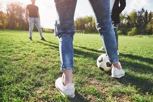 een groep vrienden in casual outfit voetballen in de open lucht. mensen veel plezier en plezier. actieve rust en schilderachtige zonsondergang foto