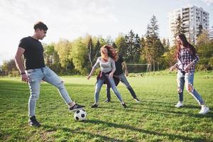 een groep vrienden in casual outfit voetballen in de open lucht. mensen veel plezier en plezier. actieve rust en schilderachtige zonsondergang foto