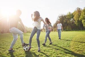 een groep vrienden in casual outfit voetballen in de open lucht. mensen veel plezier en plezier. actieve rust en schilderachtige zonsondergang
