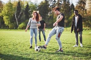 een groep vrienden in casual outfit voetballen in de open lucht. mensen veel plezier en plezier. actieve rust en schilderachtige zonsondergang foto