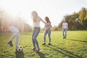 een groep vrienden in casual outfit voetballen in de open lucht. mensen veel plezier en plezier. actieve rust en schilderachtige zonsondergang foto