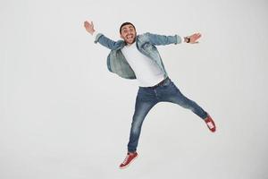 afbeelding van een vrolijke jonge man die casual gekleed over een witte achtergrond springt en een ander gebaar maakt foto