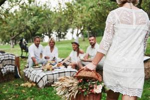 vrouw draagt mand met droge planten. groep volwassen vrienden rusten en praten tijdens het eten in de achtertuin van het restaurant foto