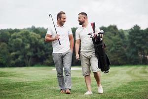 een goede tijd hebben. twee vrienden lopen door het gazon met golfuitrusting en praten foto