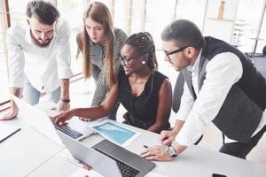 zwarte meid resultaten tonen en glimlachen. vier multiraciale werknemers hebben werk op kantoor met behulp van de laptop op tafel foto