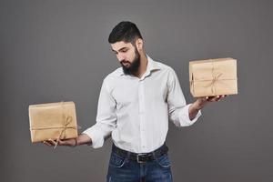 knappe romantische man kijkt naar doos en maakt een keuze. met een twee grote geschenkdoos voor zijn paar, op een grijze achtergrond.