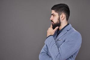 portret van freelancer man met baard in jas staande tegen een grijze achtergrond