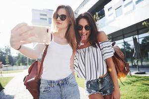 twee mooie meisjes met rugzakken lopen samen in de stad. mooie schattige vrienden delen geheimen foto