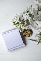 geopend notitieboekje en voorjaar bloemen Aan een wit houten bureau. foto