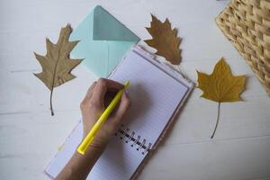 vrouw schrijven in de notebook. herfst bladeren Aan de bureaublad. foto