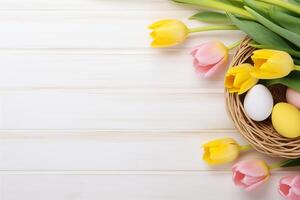 Pasen vakantie viering banier groet kaart banier met roze geschilderd eieren in vogel nest mand en geel tulp bloemen Aan wit houten achtergrond tabel textuur. foto