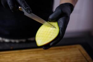 persoon met zwart handschoenen snijdend en snijden mango voor smoothie hout snijdend foto