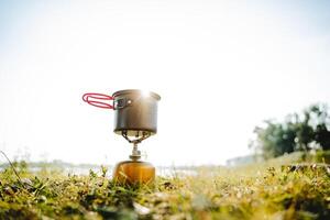 toerist gerechten staan Aan de gras tegen de achtergrond van zonsondergang in de stralen van zonlicht, de pot staat Aan een gas- brander, trekking in de Woud, compact uitrusting voor hiking, schittering foto