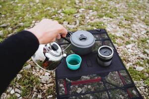 de hand- houdt de ketel, gieten thee in een mok, water giet van de tuit van de ketel, brouwen koffie Aan een wandeltocht, ochtend- ontbijt, solo reis, foto