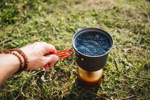 Koken in natuur, camping apparatuur, de vent kookt water in een pot Aan de brander, miniatuur borden, compact maat, trekking in de Woud. foto