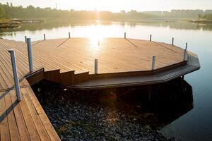 de schittering van de zon is weerspiegeld van de water, de ochtend- stadsgezicht, de houten pier Aan de rivier, de plaats van parkeren boten, de mooi dijk Aan de meer. foto