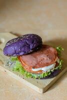 dichtbij omhoog foto van een eigengemaakt Purper hamburger geplaatst Aan een keramisch tafel