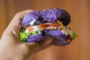 dichtbij omhoog foto van Holding een eigengemaakt Purper hamburger met een beet